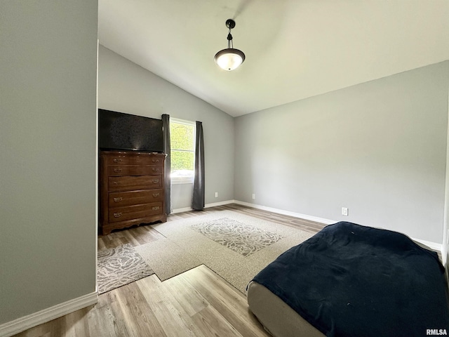 bedroom featuring baseboards, light wood finished floors, and lofted ceiling