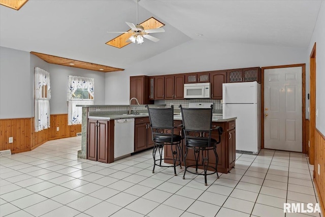 kitchen with a ceiling fan, wainscoting, a sink, wooden walls, and white appliances