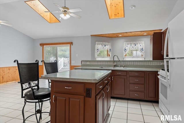 kitchen featuring a sink, vaulted ceiling with skylight, white appliances, a ceiling fan, and a wealth of natural light