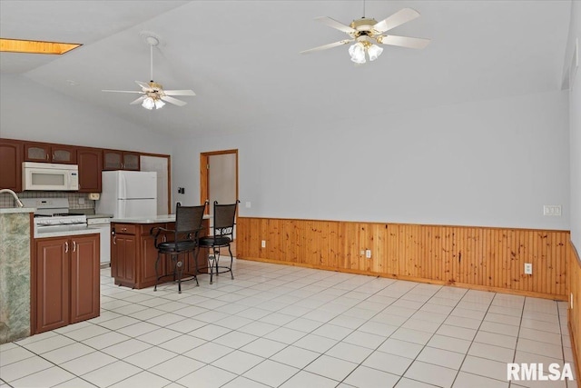 kitchen featuring a ceiling fan, light countertops, a wainscoted wall, a breakfast bar, and white appliances