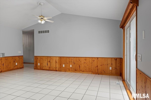 empty room featuring a ceiling fan, wainscoting, vaulted ceiling, and wooden walls