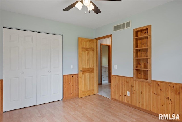 unfurnished bedroom with visible vents, wood walls, wainscoting, a closet, and light wood finished floors