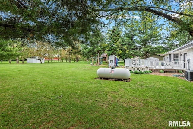 view of yard with a storage unit, a deck, an outbuilding, central AC unit, and a playground