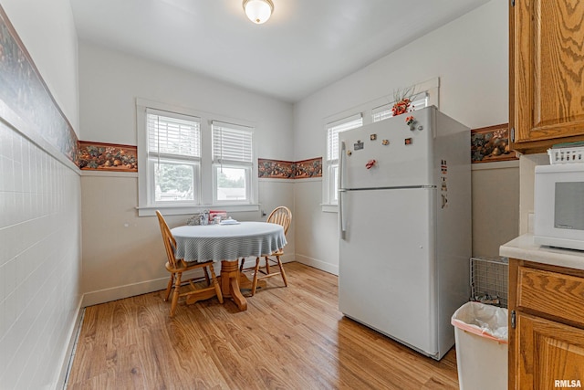 kitchen featuring white appliances, light wood-type flooring, light countertops, a wainscoted wall, and brown cabinets