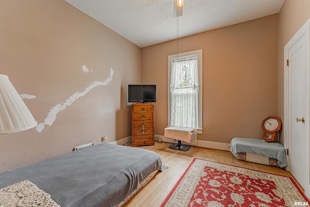 bedroom featuring wood-type flooring, a textured ceiling, baseboards, and ceiling fan