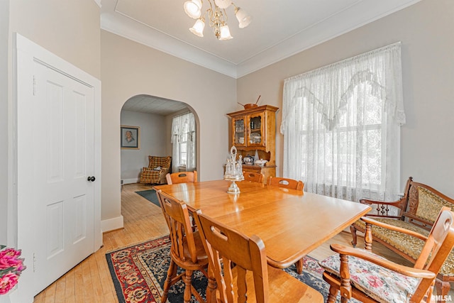 dining space with a notable chandelier, light wood-style floors, arched walkways, baseboards, and ornamental molding