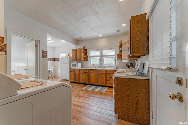 kitchen with brown cabinetry, open shelves, washer / dryer, white appliances, and light wood-style floors