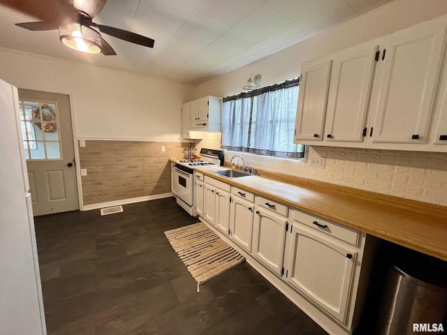 kitchen with white gas stove, a ceiling fan, visible vents, a sink, and white cabinets