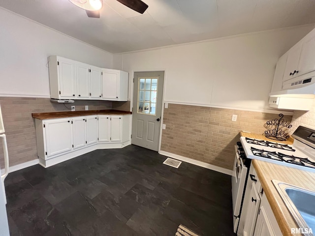 kitchen featuring a ceiling fan, brick wall, a sink, white cabinets, and white range with gas stovetop