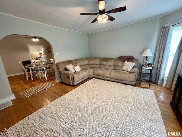 living room with baseboards, arched walkways, a ceiling fan, and wood finished floors