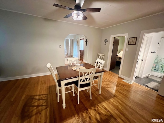 dining space with crown molding, ceiling fan, arched walkways, wood finished floors, and visible vents