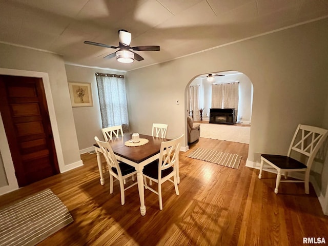 dining space featuring a ceiling fan, wood finished floors, a fireplace, baseboards, and arched walkways