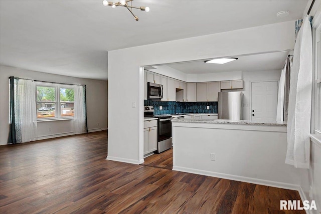 kitchen with a peninsula, a chandelier, dark wood finished floors, appliances with stainless steel finishes, and backsplash