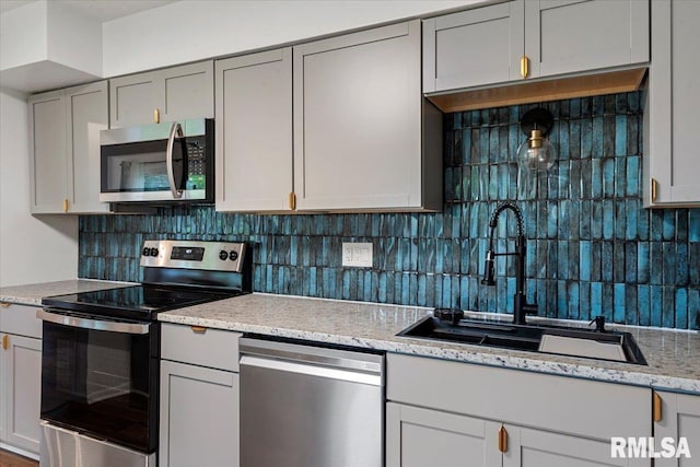 kitchen featuring a sink, decorative backsplash, stainless steel appliances, and gray cabinetry
