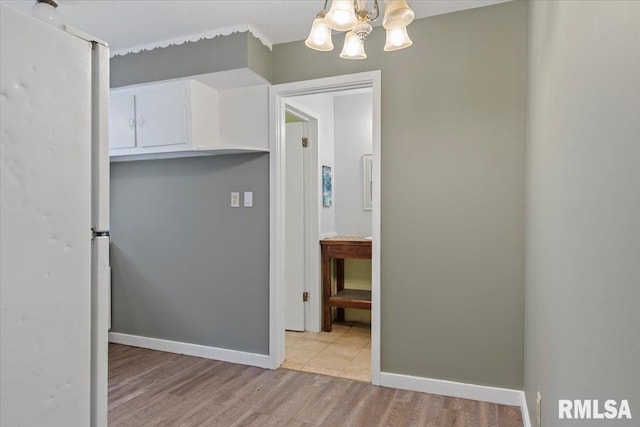 1127 N 6th St, Springfield, IL 62702 - interior space with white cabinets, light wood-style floors, a chandelier, freestanding refrigerator, and baseboards