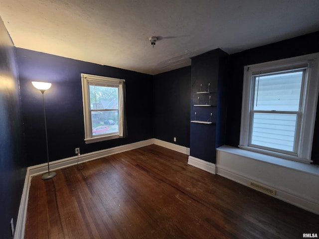 empty room featuring baseboards, visible vents, and wood finished floors