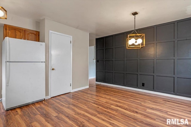 unfurnished dining area with an inviting chandelier, baseboards, a decorative wall, and wood finished floors