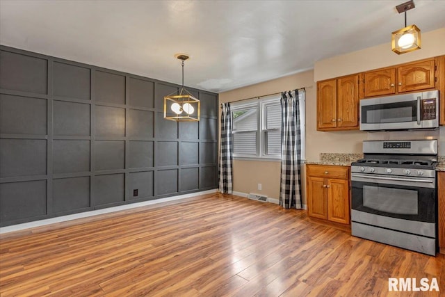kitchen featuring a decorative wall, brown cabinetry, light wood-style flooring, stainless steel appliances, and baseboards