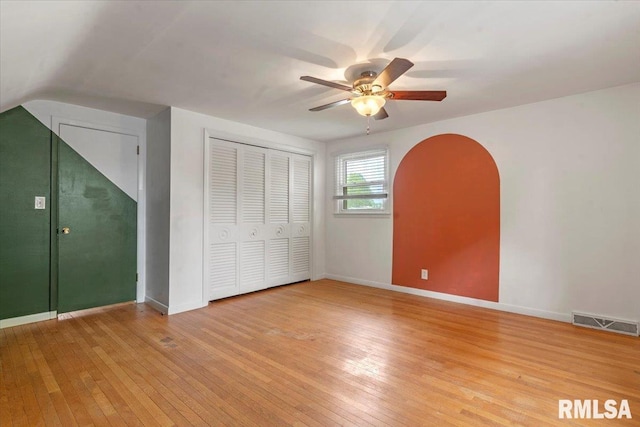 unfurnished bedroom featuring visible vents, arched walkways, baseboards, a closet, and light wood-style floors