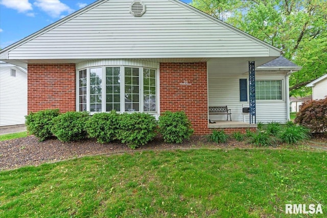 exterior space featuring a porch, brick siding, and a front yard