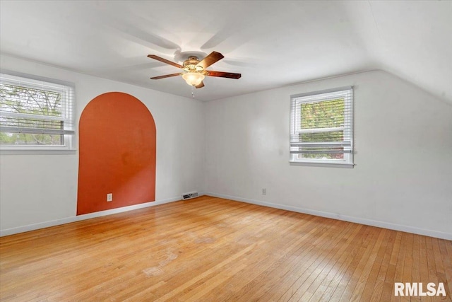 spare room featuring ceiling fan, arched walkways, light wood-style flooring, vaulted ceiling, and visible vents