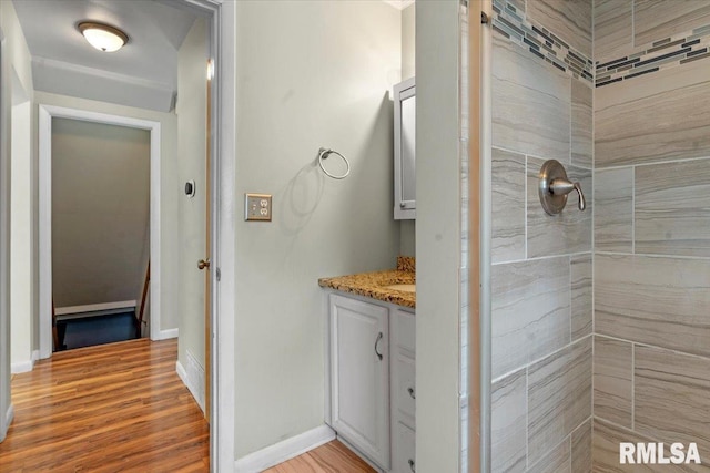 full bath featuring wood finished floors, baseboards, tiled shower, and vanity