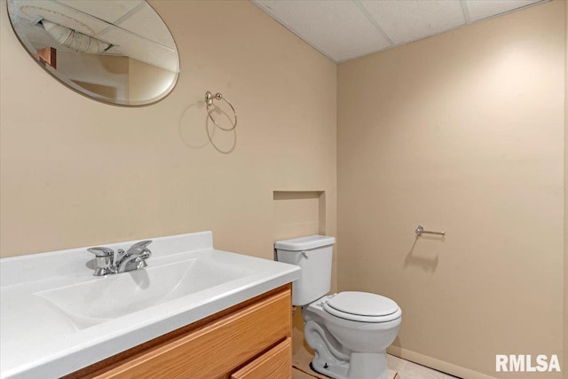 bathroom with vanity, toilet, baseboards, a paneled ceiling, and tile patterned floors