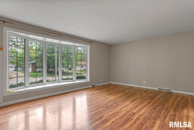 unfurnished room featuring visible vents, wood finished floors, and a wealth of natural light