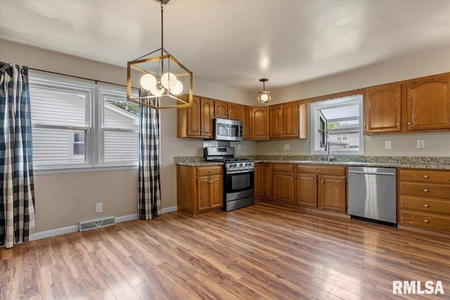 kitchen with brown cabinetry, stainless steel appliances, wood finished floors, and visible vents