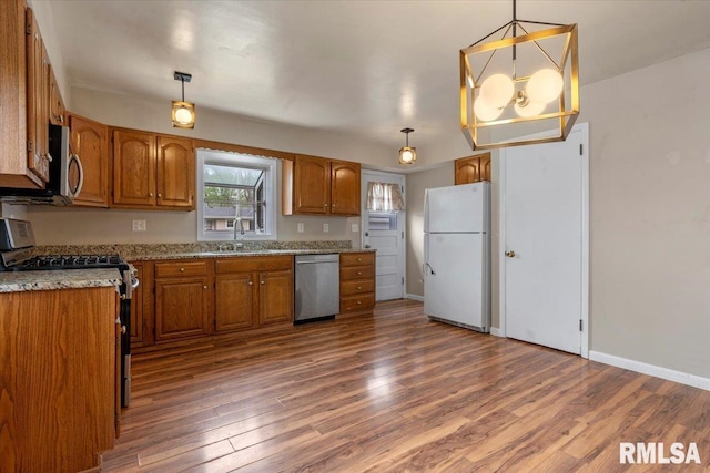 kitchen featuring stainless steel appliances, decorative light fixtures, brown cabinetry, and wood finished floors