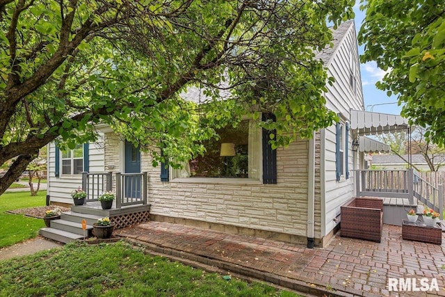 obstructed view of property featuring a patio area, stone siding, and a front lawn