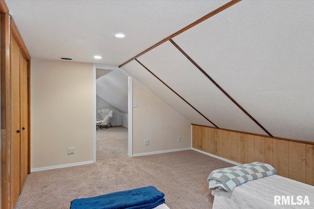 carpeted bedroom with a textured ceiling, vaulted ceiling, baseboards, wooden walls, and recessed lighting