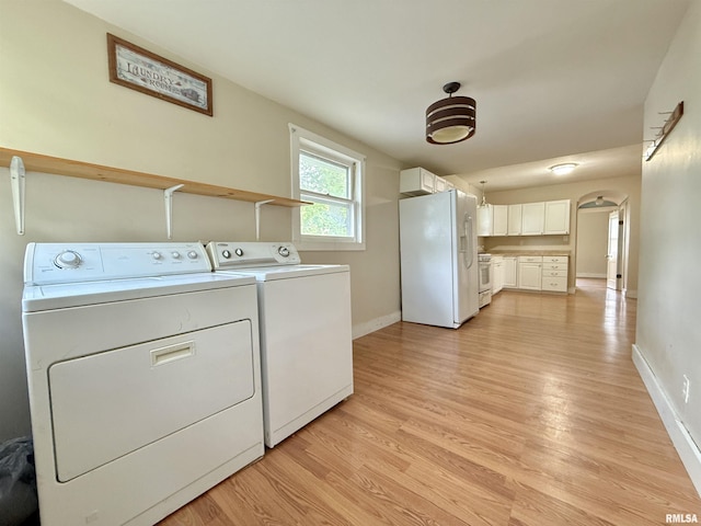 laundry area featuring light wood-style floors, baseboards, arched walkways, and washer and clothes dryer