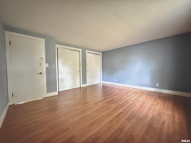 unfurnished bedroom featuring multiple closets, baseboards, and wood finished floors
