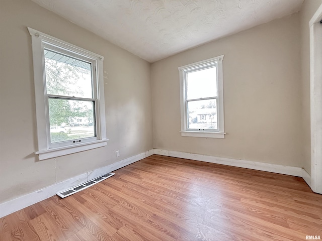 empty room featuring visible vents, baseboards, a healthy amount of sunlight, and light wood-style floors