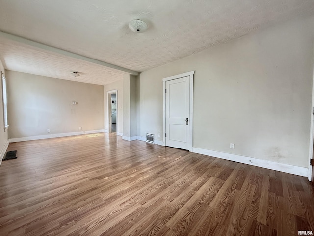 spare room featuring baseboards, a textured ceiling, wood finished floors, and visible vents