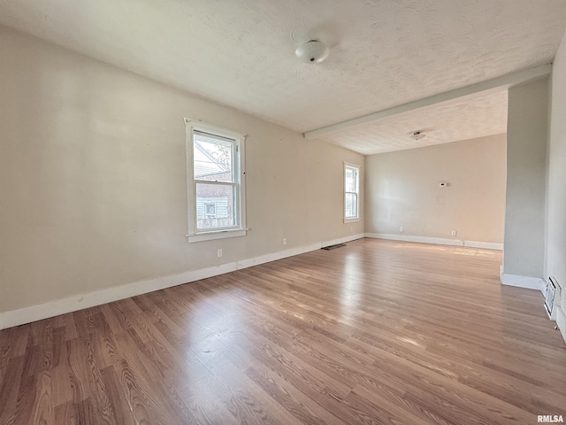 empty room featuring baseboards, a textured ceiling, visible vents, and light wood-style flooring