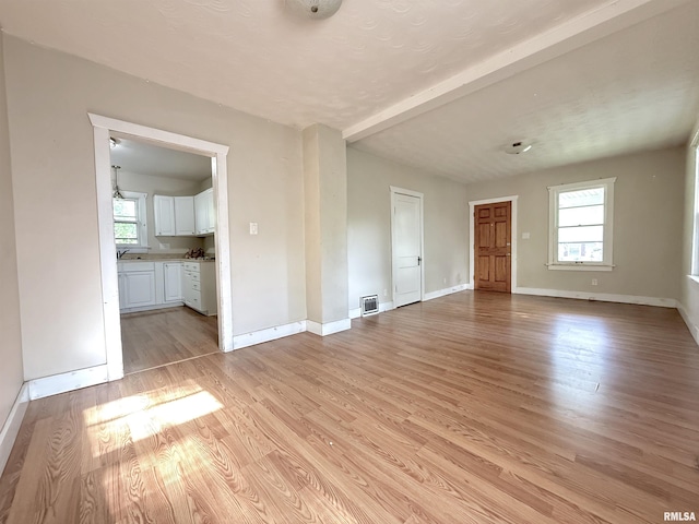 unfurnished living room featuring baseboards, light wood-type flooring, beam ceiling, and a wealth of natural light