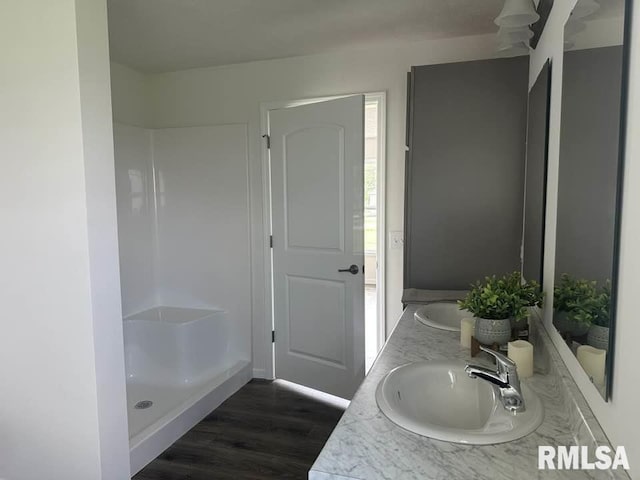 bathroom featuring double vanity, walk in shower, a sink, and wood finished floors