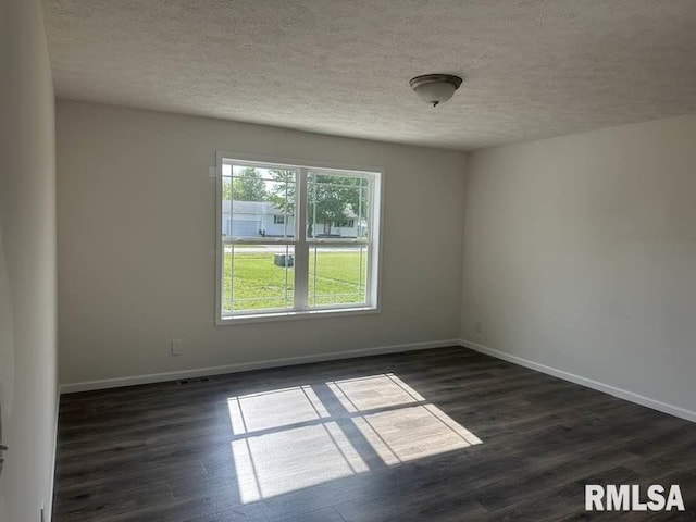 empty room featuring dark wood-style flooring, a textured ceiling, visible vents, and baseboards