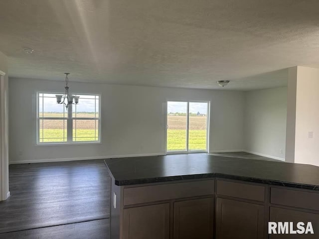 kitchen featuring dark countertops, dark wood finished floors, baseboards, open floor plan, and an inviting chandelier