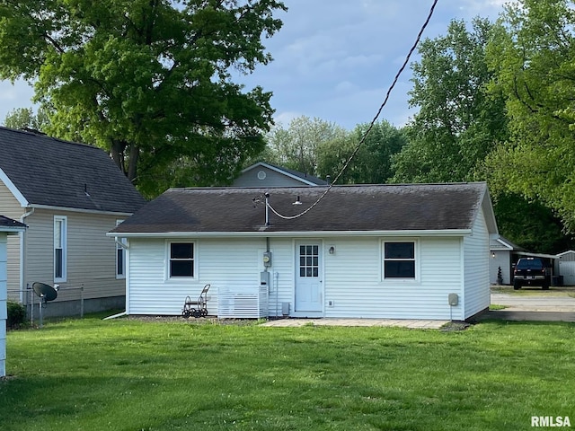 rear view of property featuring a lawn, roof with shingles, and fence