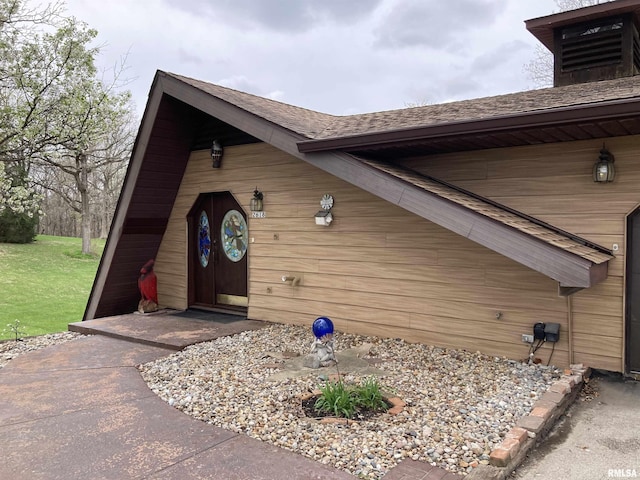 view of exterior entry featuring a yard and roof with shingles