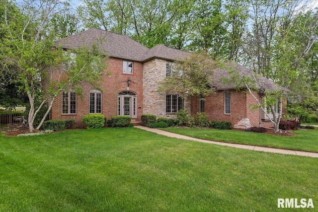 view of front of property featuring a shingled roof, brick siding, and a front yard
