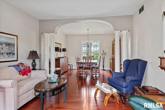 living area featuring dark wood-style flooring, visible vents, a chandelier, arched walkways, and ornate columns