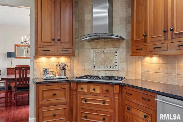 kitchen featuring wall chimney range hood, brown cabinets, appliances with stainless steel finishes, and decorative backsplash