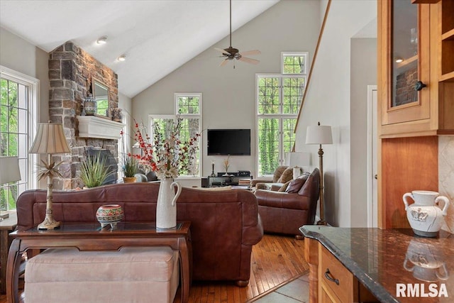 living area featuring a fireplace, ceiling fan, light wood-style flooring, and high vaulted ceiling