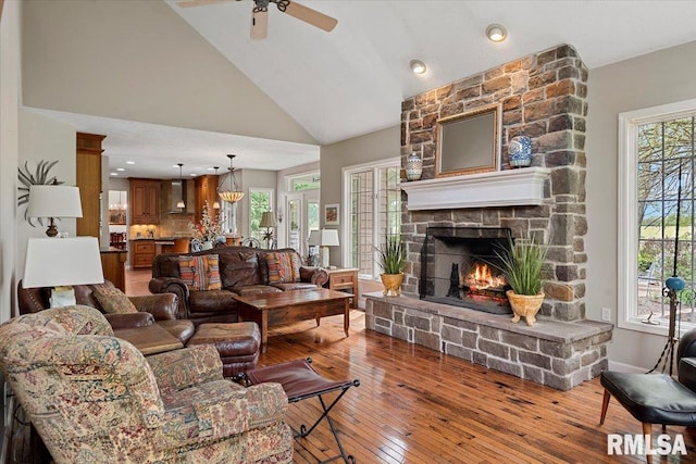 living room featuring lofted ceiling, hardwood / wood-style floors, a fireplace, a ceiling fan, and baseboards