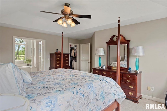 bedroom with a closet, light colored carpet, a ceiling fan, a walk in closet, and baseboards