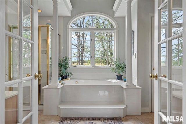 bathroom featuring tile patterned floors, french doors, ornate columns, and a garden tub